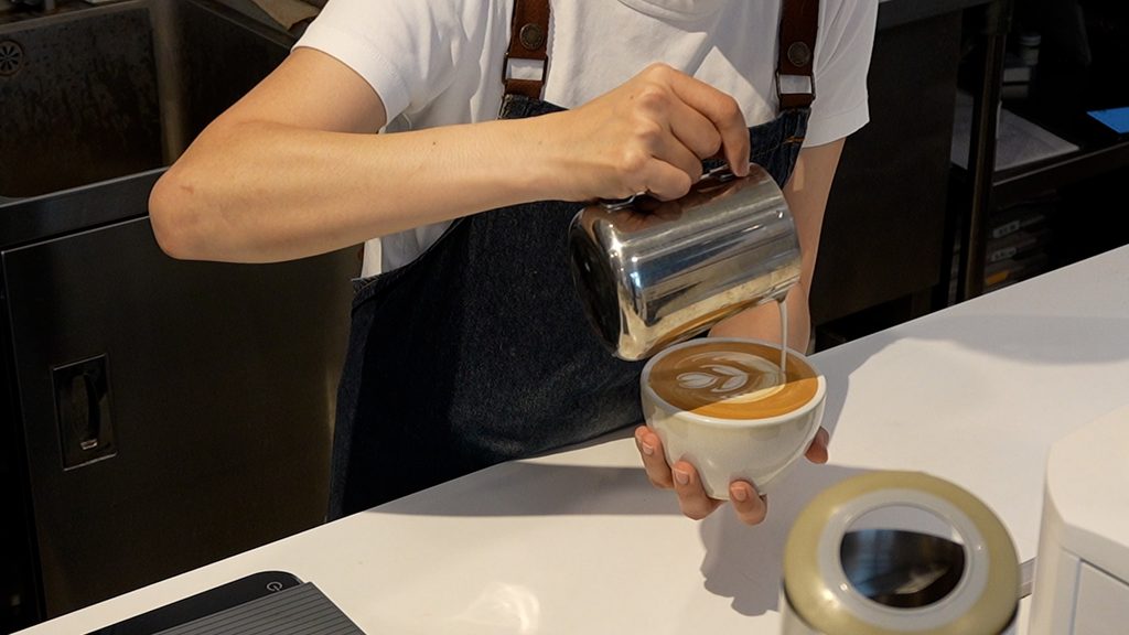 L'USiNE Café 店長 Miru 正在吧檯專注進行咖啡拉花，展現早午餐咖啡廳的職人專業度